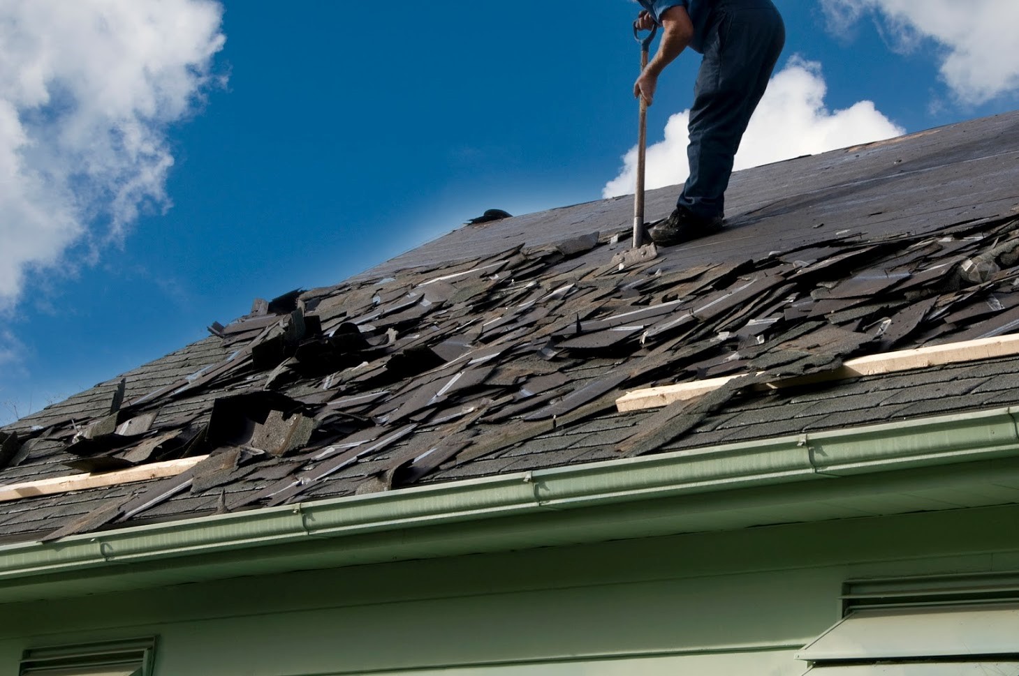 Worker removing roofing shingles from a roof